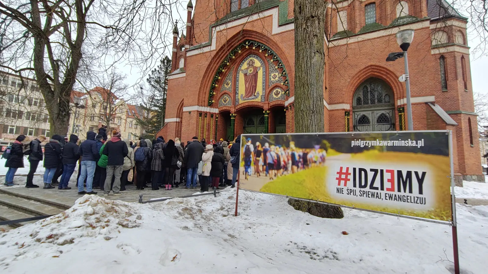 Turyści zsłuchani w opowieści przewodnika po OLsztynie pod kościołem NSPJ